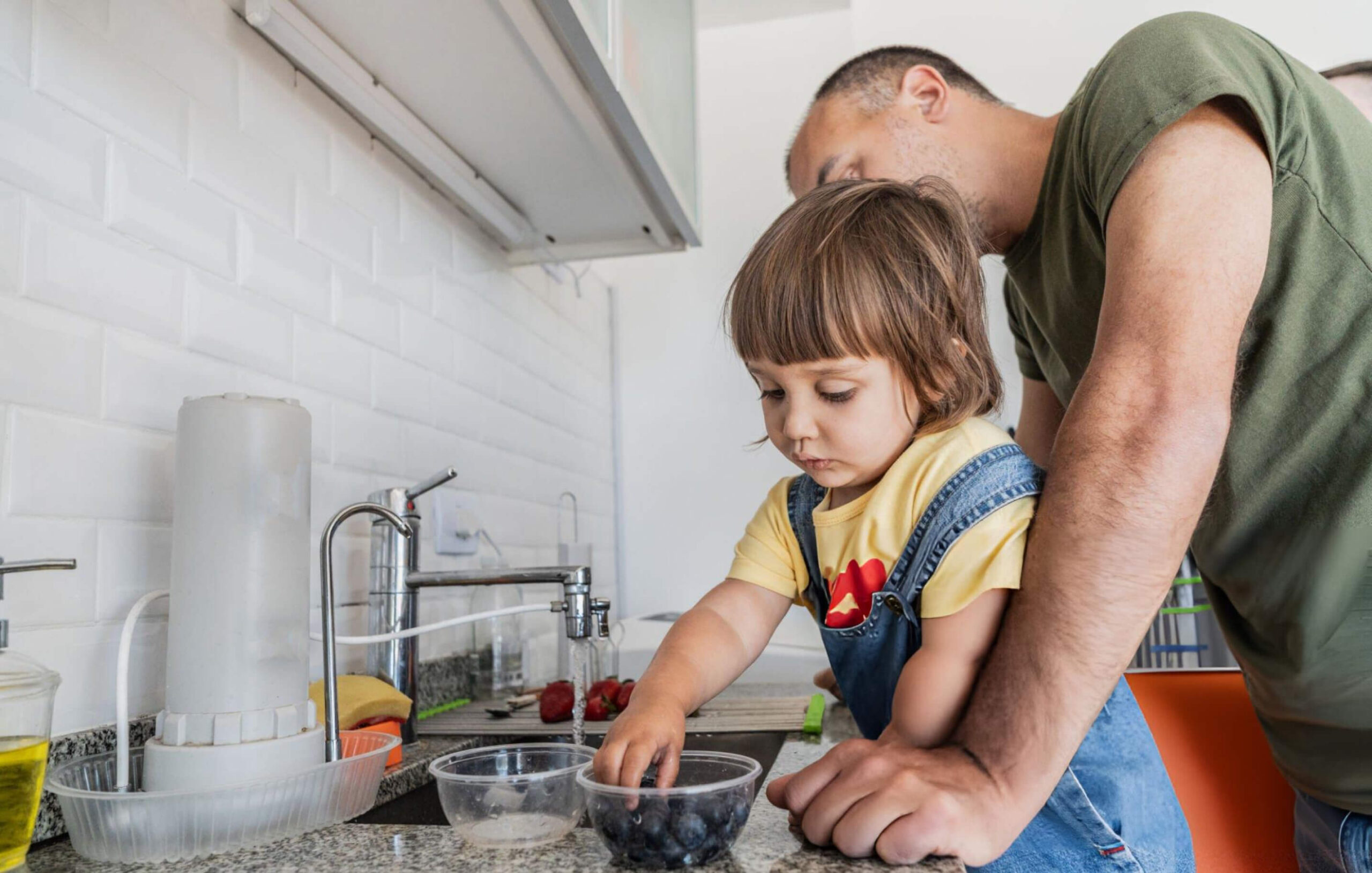 Father and daughter washing fruits in the sink at home